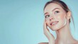 © atipong - Skincare. Woman with beautiful face touching healthy facial skin. Beautiful portrait of smiling Asian girl model with natural makeup enjoys glowing hydrated skin on blue background closeup. High