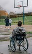 © goami - disabled boy in a wheelchair watches a basketball game on an outdoor court, scene reflects desire for sports and social inclusion