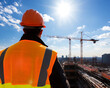 © Shining Pro - Construction worker observes workplace activity under a bright sun, showcasing safety and teamwork at a building site.