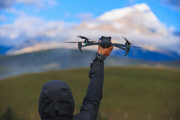 Wall Mural - Photographer taking photo of snow capped mountain with a drone on high altitude grassland mountain top