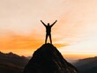 © Aleksandra - A silhouette of a person standing on a mountain peak with arms raised in victory backlit by a golden sunset The image conveys success achievement and triumph over challenges The background is expansiv