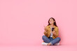 © New Africa - Smiling young woman with smartphone pointing at something on pink background. Space for text