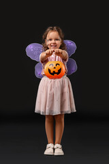 Cute girl with pumpkin bucket dressed like fairy for Halloween celebration on black background