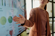 © pressmaster - Person presenting data on an interactive screen displaying various growth metrics and charts in modern office environment