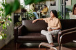 © pressmaster - Office with employees engaging in tasks and relaxing on a brown sofa while holding a mug, with greenery enhancing the relaxed atmosphere