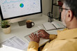 © pressmaster - Detail of person analyzing financial data on desktop computer with charts and graphs visible on screen, working in bright and organized office environment, drinking coffee