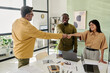 © pressmaster - Smiling business team congratulating each other with handshake in modern office with laptops and documents scattered on table