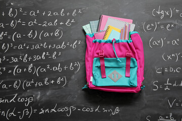 Wall Mural - Colorful school backpack with notebooks and pencils on black chalkboard painted with formulas