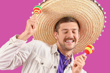 Wall Mural - Young Mexican man in sombrero and with maracas on magenta background