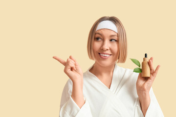 Wall Mural - Beautiful mature woman with bottle of essential oil pointing at something against color background