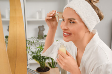 Canvas Print - Beautiful woman applying serum near mirror in bathroom, closeup