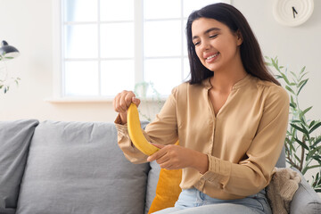 Wall Mural - Young woman with banana sitting on sofa at home