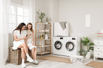 Poster - Female students using mobile phones in dorm laundry room