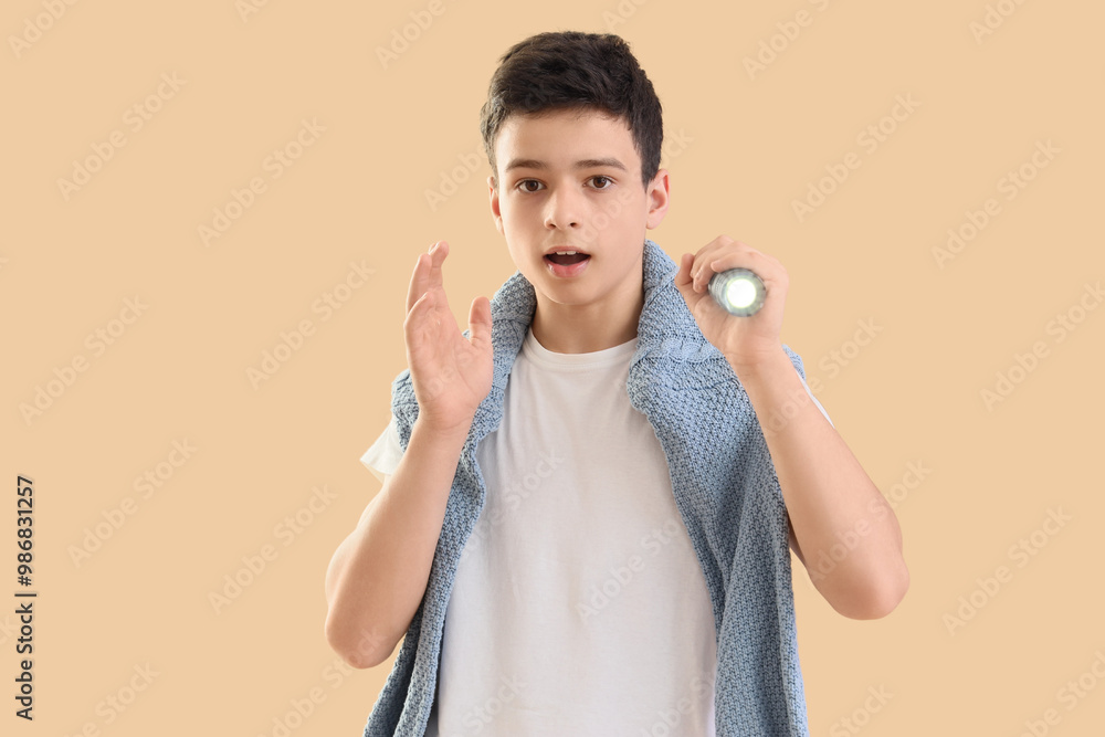 Shocked teenage boy with shining flashlight on beige background