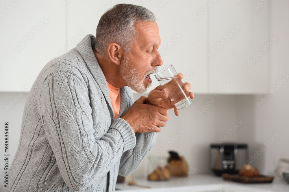 Senior man suffering from Parkinson syndrome drinking water in kitchen