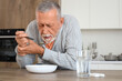 © Pixel-Shot - Senior man suffering from Parkinson syndrome eating soup at table in kitchen