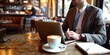 © kwanchaift - A businessman in a cozy coffee shop, using his laptop to send emails, with a latte and notebook beside him, representing the flexibility of modern work environments
