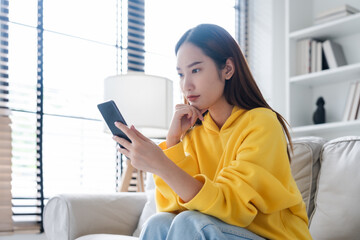 Bad news on device screen. Upset asian woman frustrated by problem with work or relationships, sitting on couch, feeling despair and anxiety, loneliness, having psychological trouble