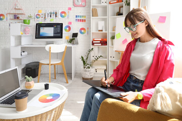 Wall Mural - Female graphic designer working with tablet in armchair at office