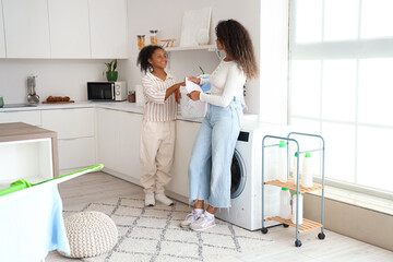 Wall Mural - African-American woman and her daughter doing laundry at home