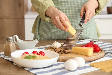 Wall Mural - Woman grating cheese onto board at table in kitchen, closeup