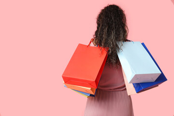 Wall Mural - Young African-American woman with shopping bags on pink background, back view