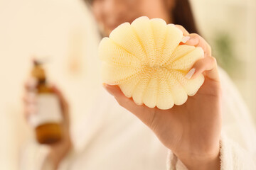 Poster - Beautiful young woman in bathrobe with bottle of cosmetic product and sponge after shower at home, closeup