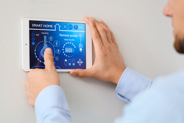 Canvas Print - Young man using smart home control panel on light wall in room, closeup