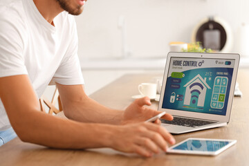 Canvas Print - Young man with smart home application on gadgets in kitchen, closeup