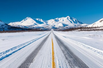 Snow-covered road leading through a mountainous winter landscape under a clear blue sky.