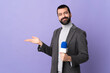 © luismolinero - Adult reporter man with beard holding a microphone over isolated purple background extending hands to the side for inviting to come