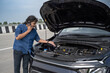 © Ojas - Young Indian woman standing by her car with the hood open, gazing at the damaged engine in frustration as she tries to figure out the problem