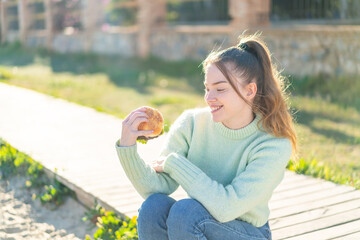 Wall Mural - Young pretty girl holding a burger at outdoors with happy expression