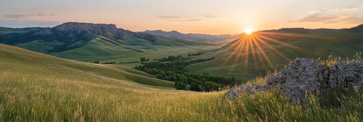 Wall Mural -  The sun sets over mountains, a grassy field lies beneath, a rock outcropping highlights the foreground