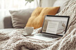 © Irina B - A laptop with a cup of tea on a knitted blanket in a cozy home setting, soft and warm atmosphere for casual browsing or working from home, with natural light filtering in.