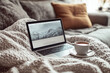 © Irina B - A cozy setup featuring a laptop displaying a webpage with a mountain scene, placed on a knitted blanket with a cup of tea beside it, creating a warm and relaxing atmosphere.