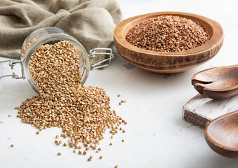 Wall Mural - Bowl of brown dry raw organic buckwheat seeds with green seeds in glass jar on light table.Macro.