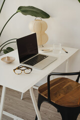 Wall Mural - minimalist home office with laptop, glasses, and lamp on white desk surrounded by green plants. mode