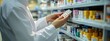 © Lars - The photo shows the hand of an employee in a white medical uniform holding and examining medicine on shelves, which are located next to them