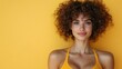 © JoxyAimages - Portrait of a smiling woman with curly hair wearing a yellow top and standing against a vibrant yellow background. Her expression exudes warmth and confidence.