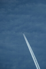 Wall Mural - Airplane in the blue sky with contrail in the clouds.