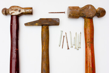 Photo of three hammers and some rusty nails. These three hammers have wooden handles and are also old and rusty tools.  