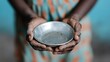 © JoxyAimages - A pair of hands, weathered and thoughtful, holding an empty metal bowl, symbolizing hunger and expectation, set against a muted background to highlight the solemn moment.