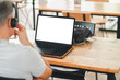 © Satori Studio - Man with headphones working on a laptop with a blank screen in a modern cafe. Wooden table and bright interior.