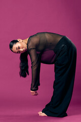 Wall Mural - Asian woman in black pants and sheer top bending over on a purple background with hands on knees and head tilted to the side