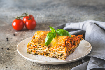 Italian lasagna with tomato sauce, spinach and cheese on light concrete background