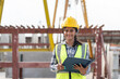 © Supachai - Asian woman engineer holding document smiling at construction site. Confident female Indian wearing protective helmet and vest working in factory making precast concrete wall for real estate housing.