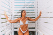 © svetograph - A woman in a bikini poses in front of a white structure with a shower. She is holding a glass of wine and she is enjoying herself