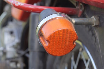 one small round red glass headlight turn signal on a old motorcycle on the street