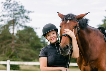 Woman with a black helmet stroking a beautiful chestnut horse head, close up shot. Human and animal relation concept.